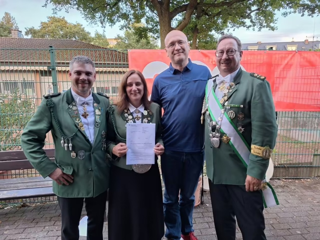 Vier Personen beim Schützenfest der Adlerschützen Zollstock; eine Frau hält den Förderbescheid in der Hand.
