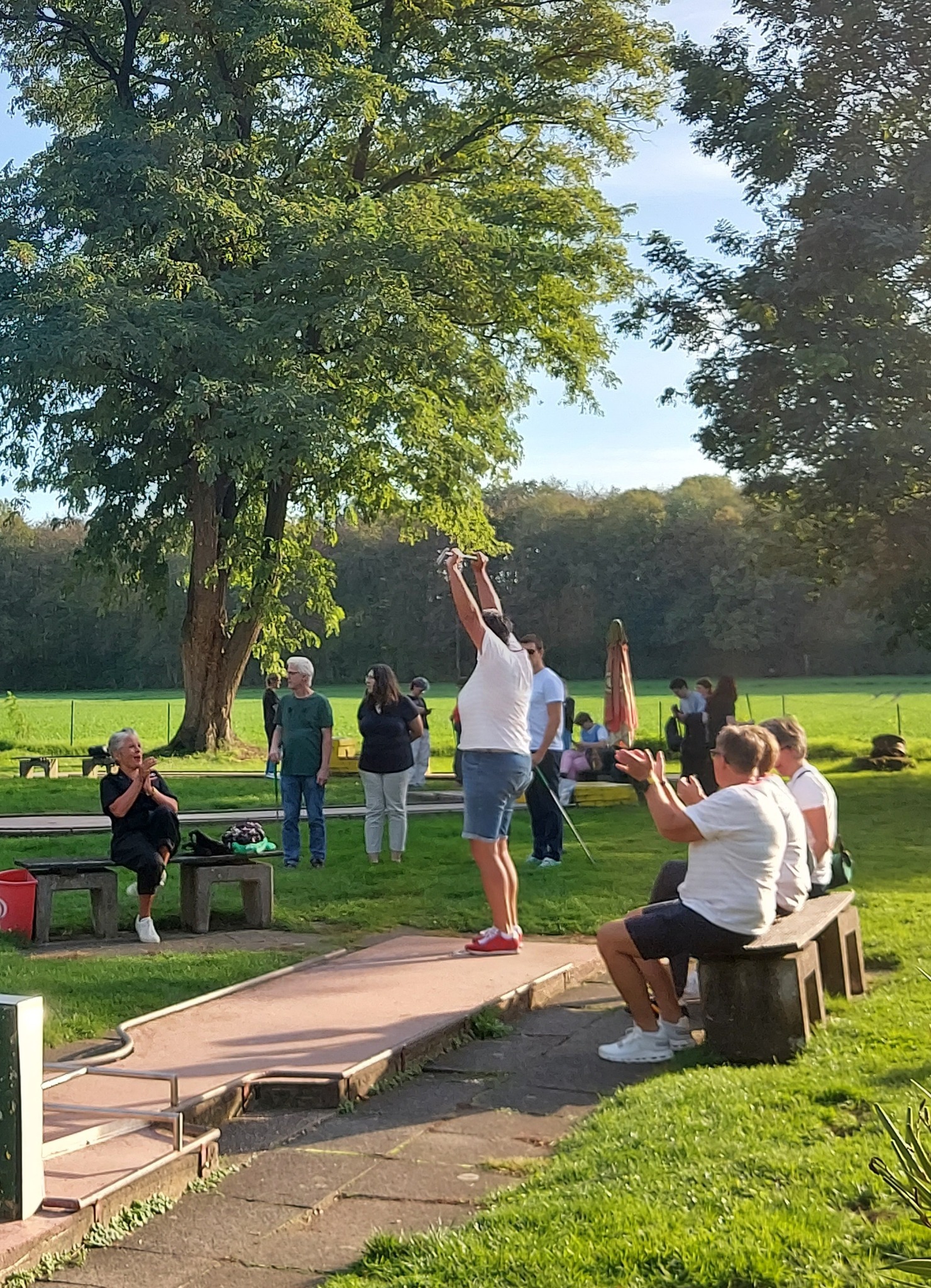 Teilnehmerin reißt beim Queer-Minigolf-Turnier in Rodenkirchen die Arme hoch, Publikum applaudiert