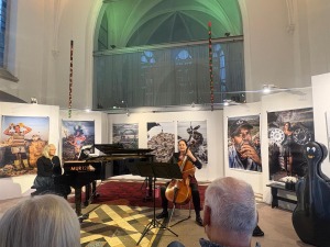 Konzert „Wunschpunsch … oder Ablage P“ mit Klavier und Violoncello vor großformatigen Fotoporträts